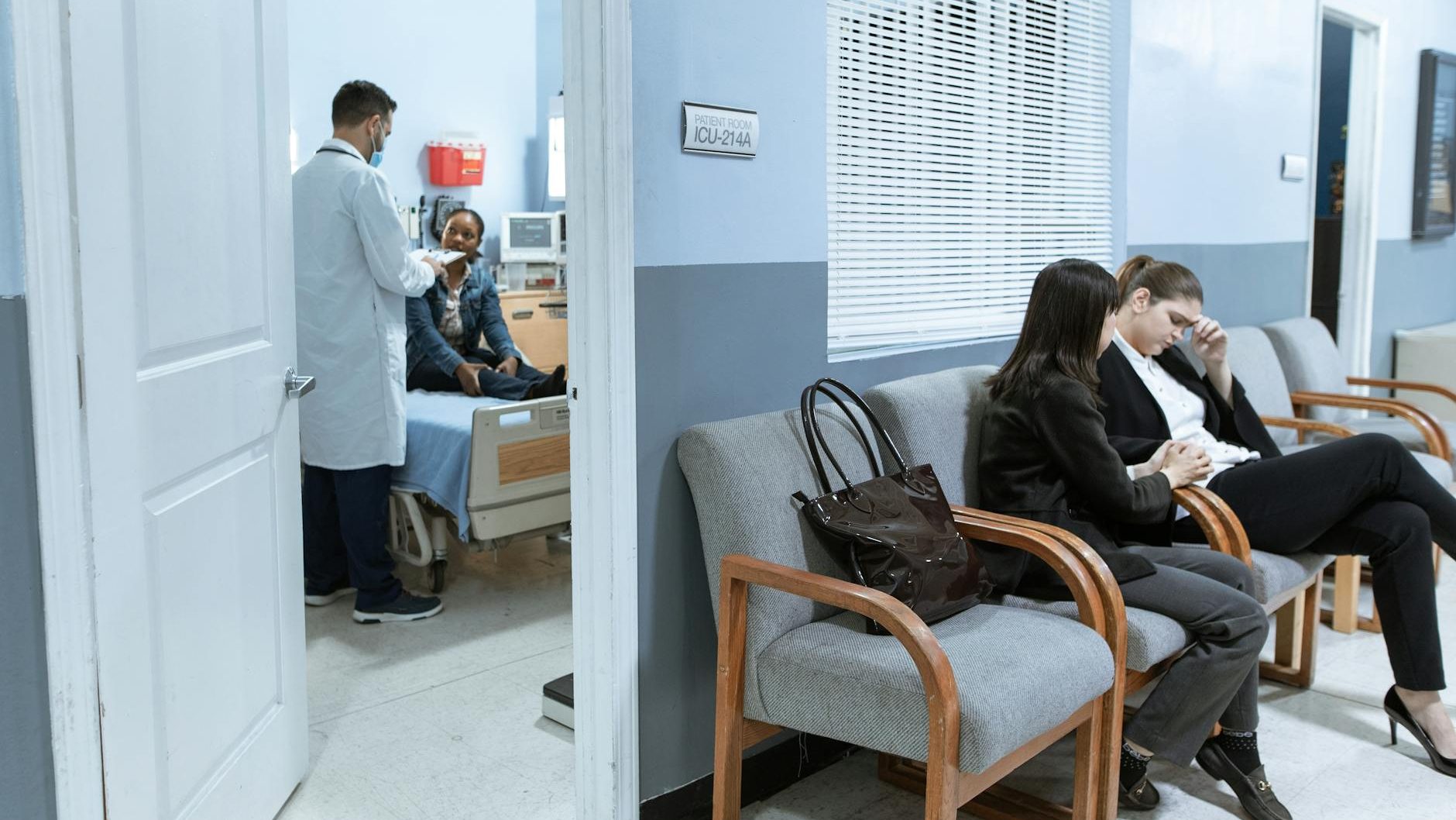 two patients wait in a waiting room while a doctor attends to another patient.
